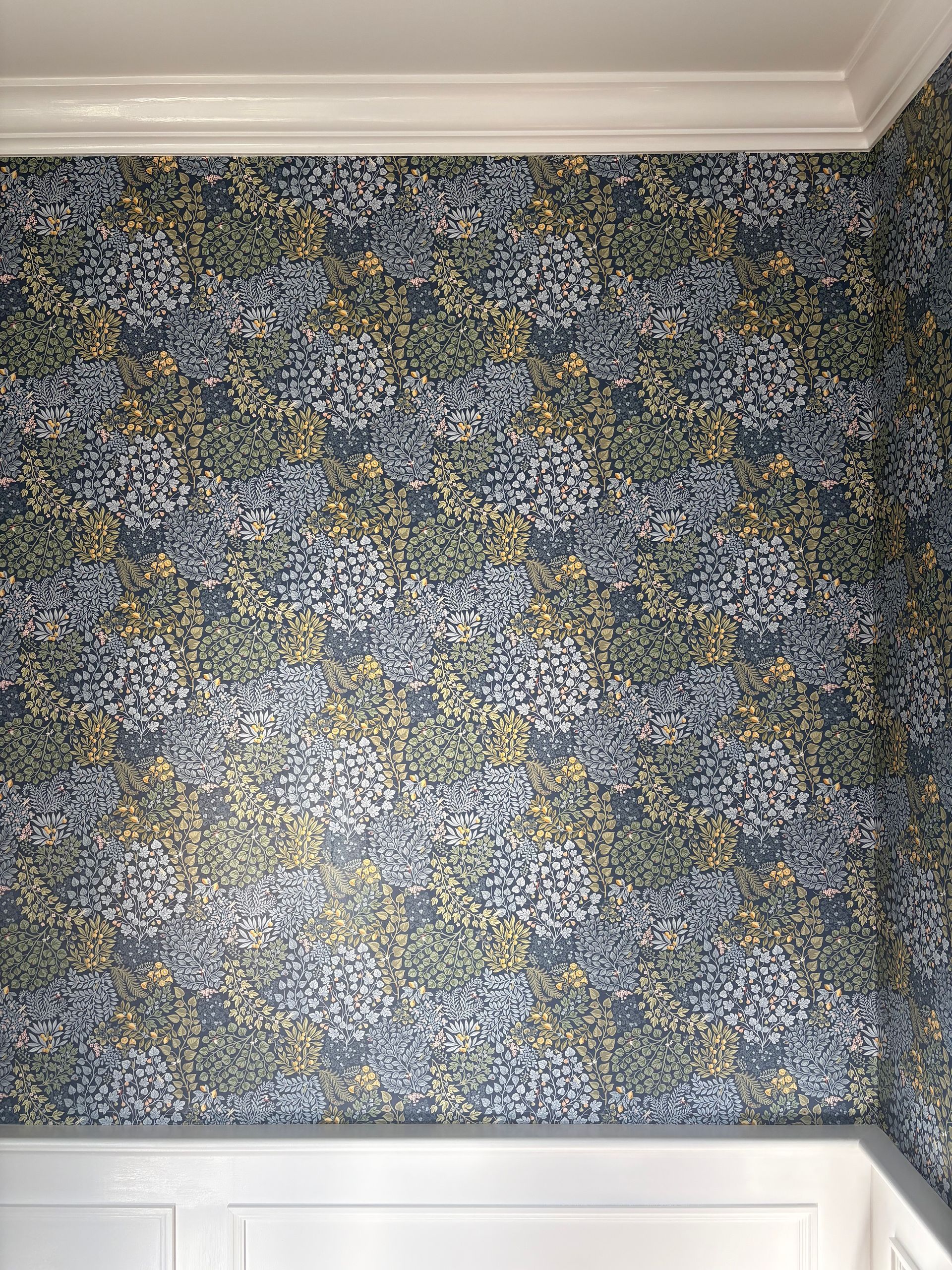 Wall section with symmetrical floral wallpaper in blue, green, and yellow tones, bordered by white crown molding and wainscoting.