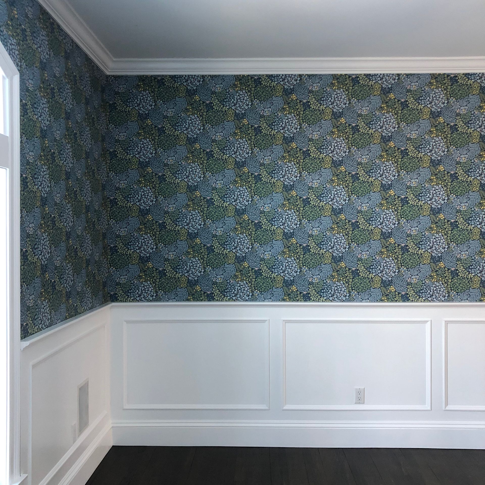 Room corner with vibrant floral wallpaper, white wainscoting, and crown molding, showcasing traditional design with decorative contrast.