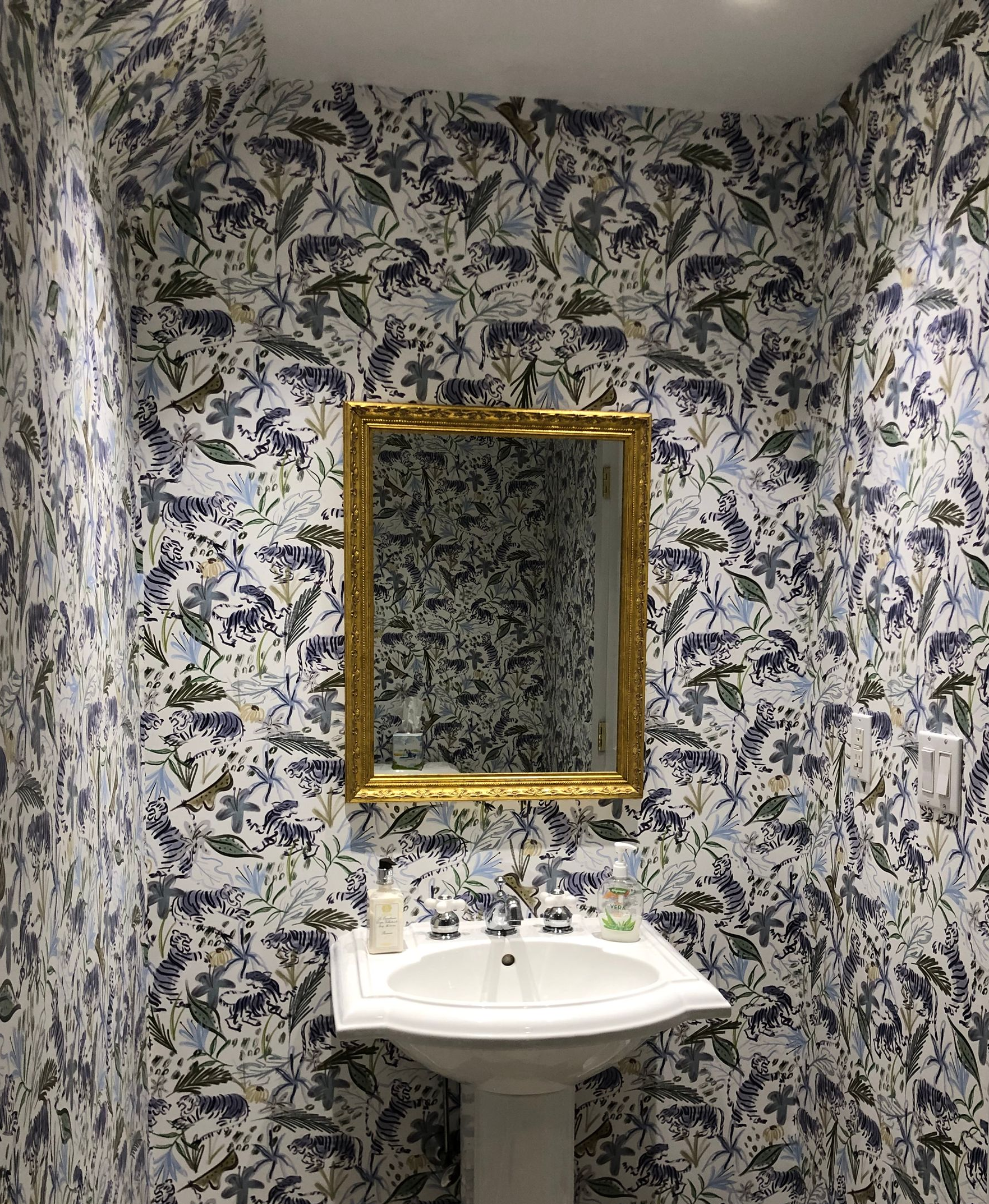 Bold floral wallpaper wraps powder room with mirror and sink.