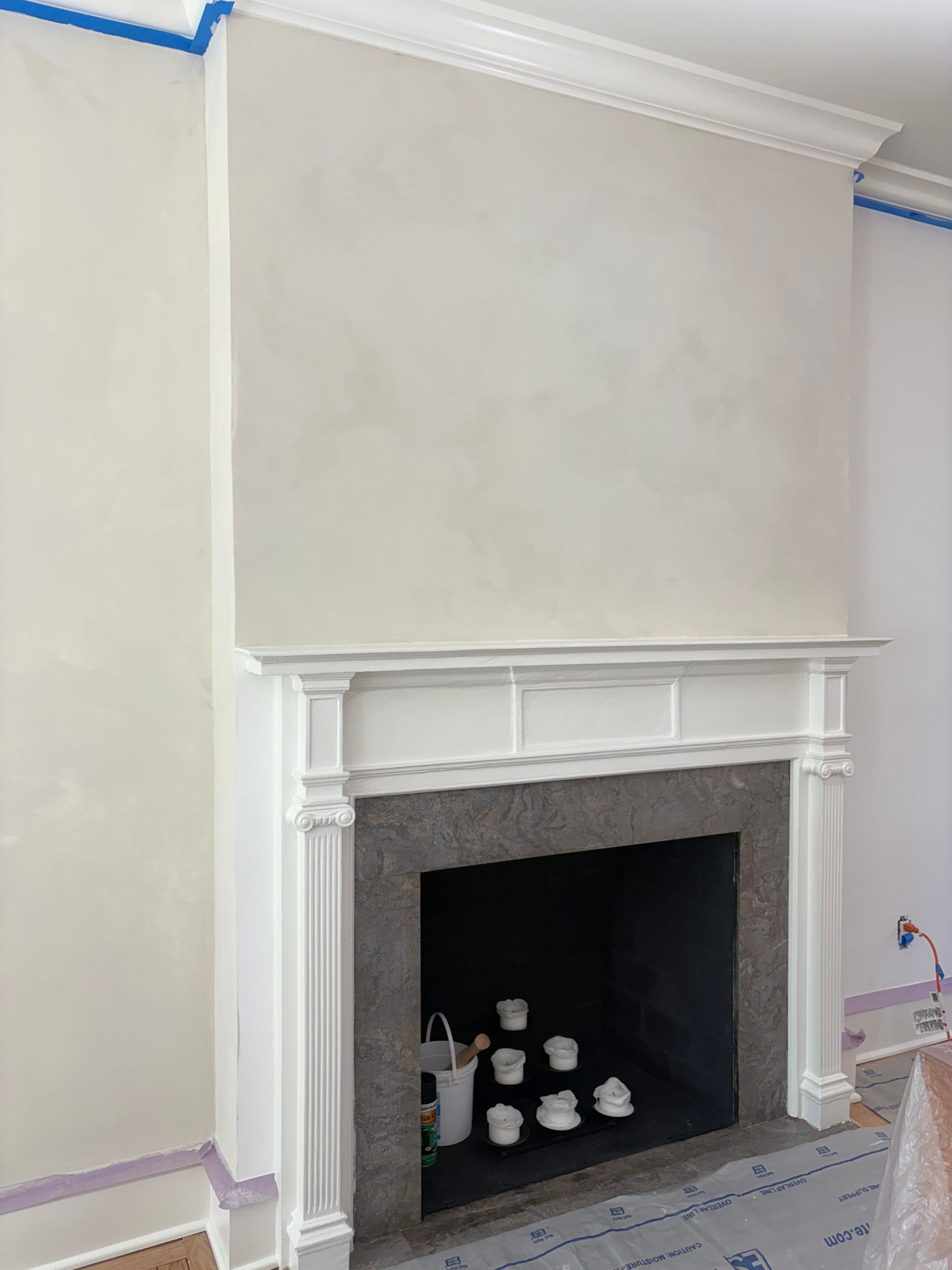 White fireplace mural with fluted columns and painting supplies nearby.