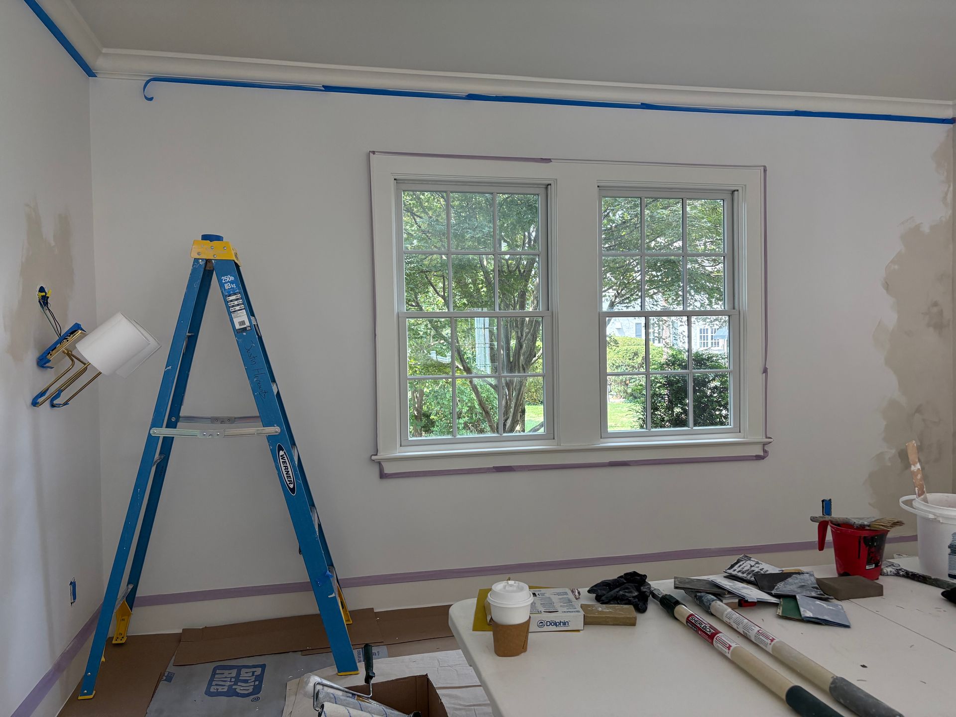 Room painting in progress with ladder, window, and paint tools.