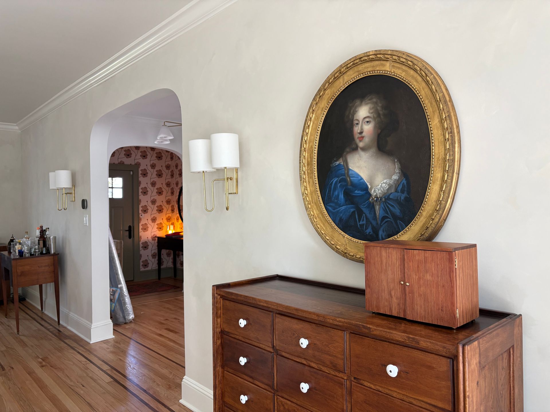 gold-framed portrait above dresser with arched doorway.