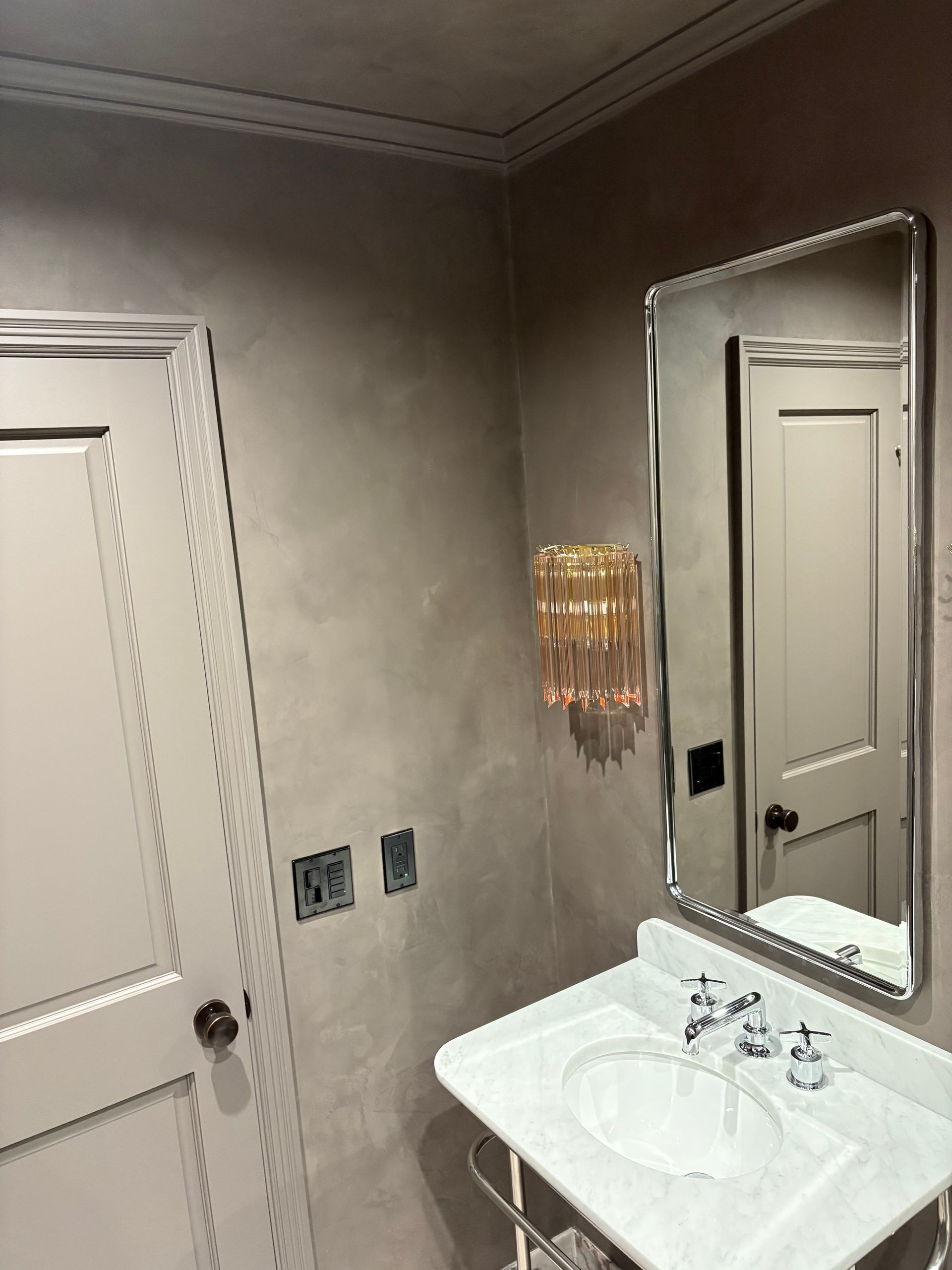 Bathroom with marble sink, chrome mirror, and warm lighting.