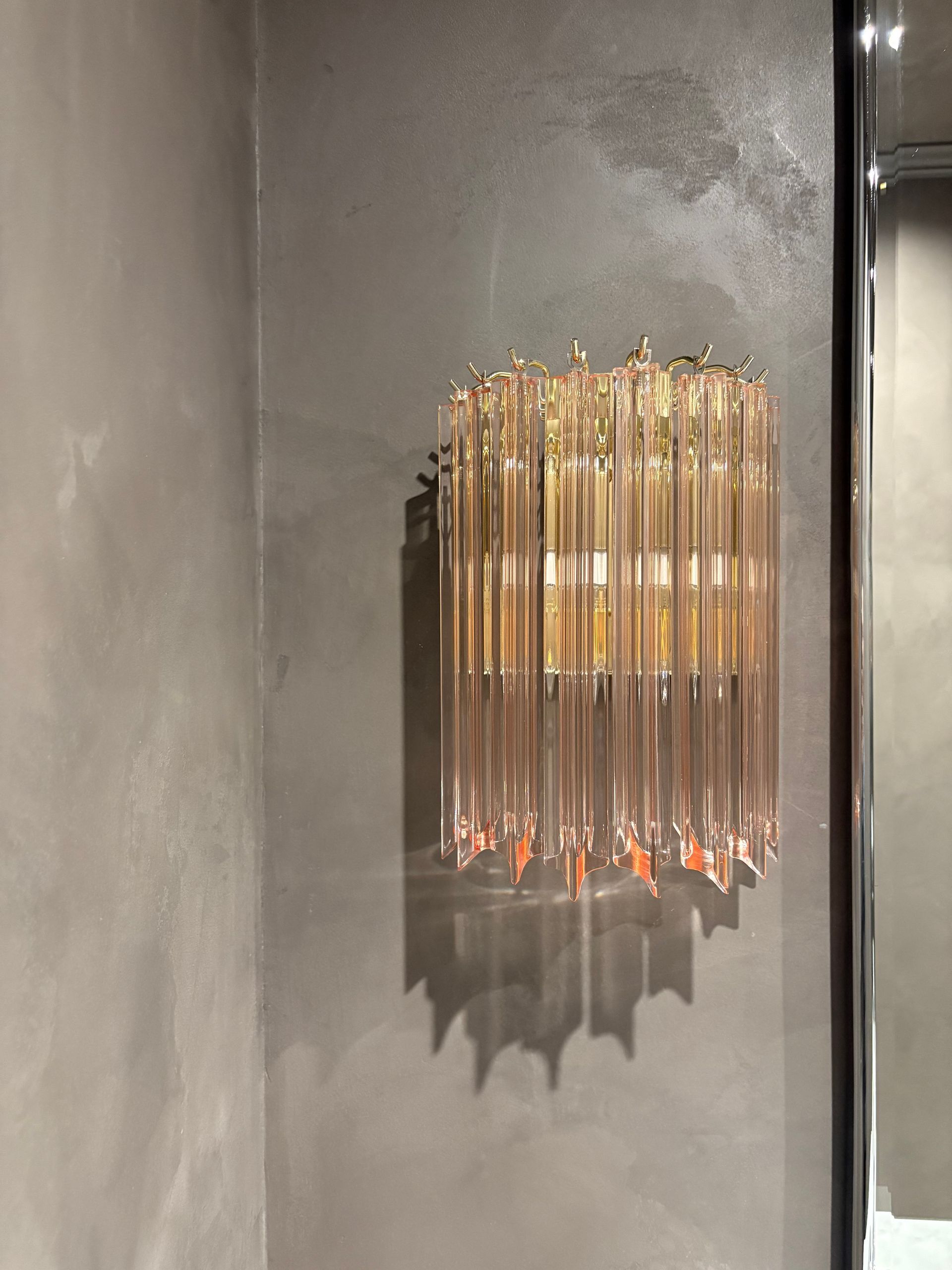 Decorative light fixture with pink glass prisms and brass frame.