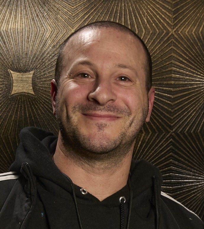 Justin in black hoodie standing in front of a textured wall with geometric diamond pattern.
