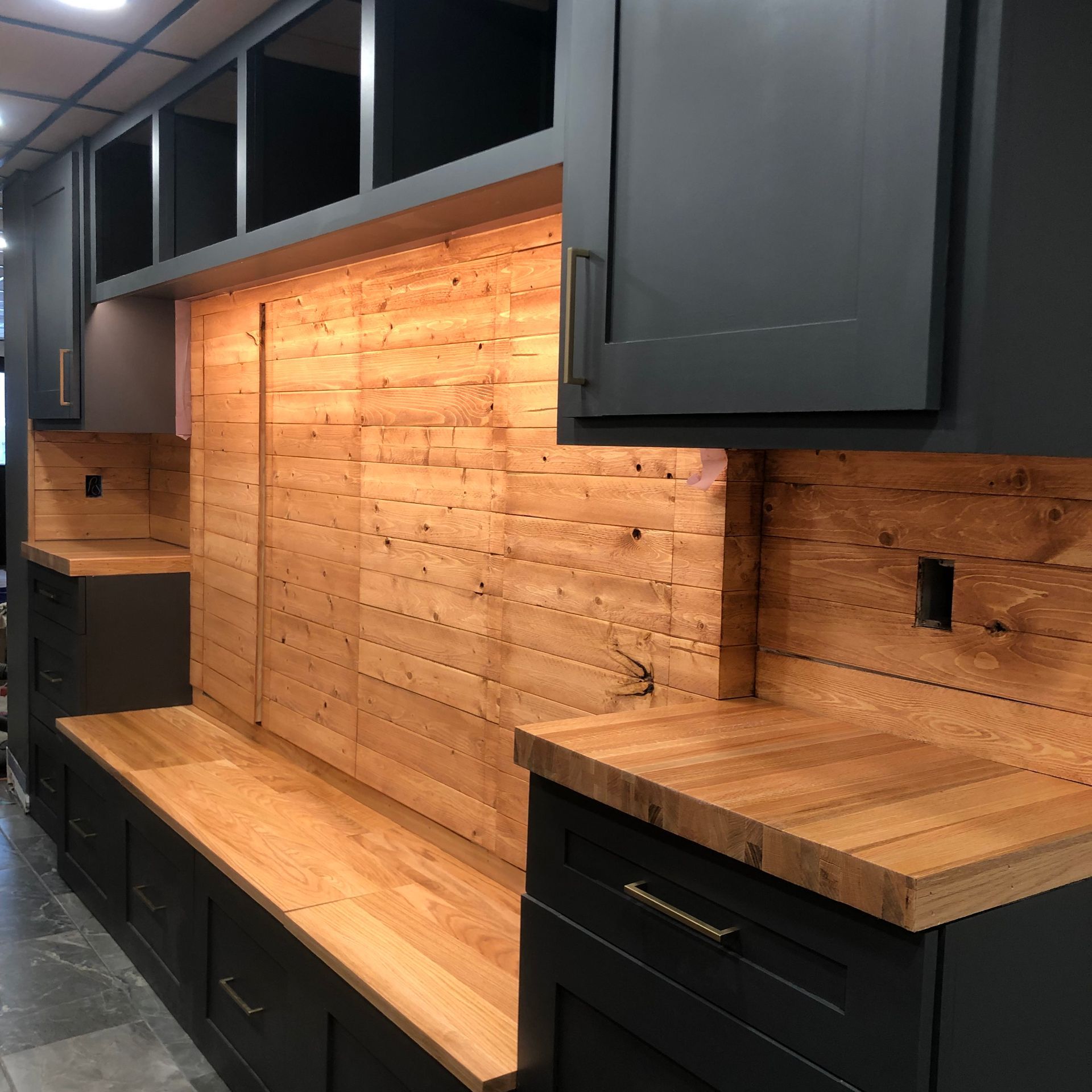 Kitchen with dark cabinets, wood backsplash, and stone floor.