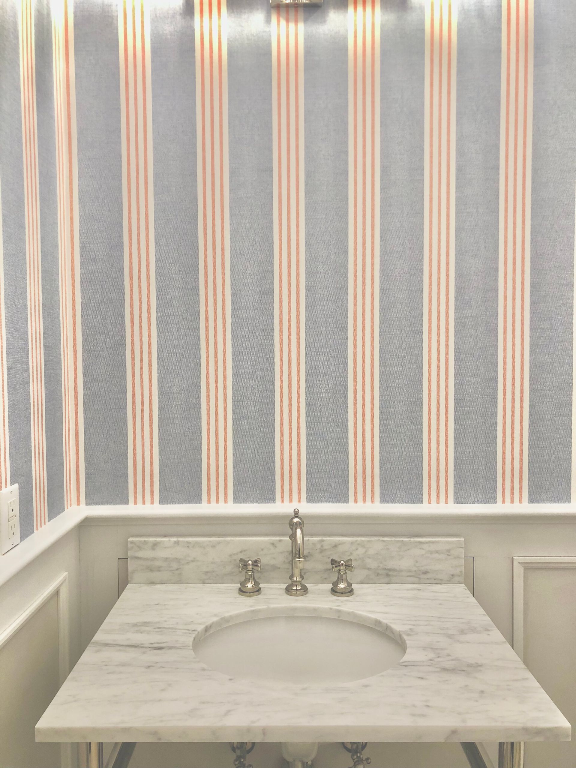Bathroom with striped wallpaper, marble sink, and wall light.