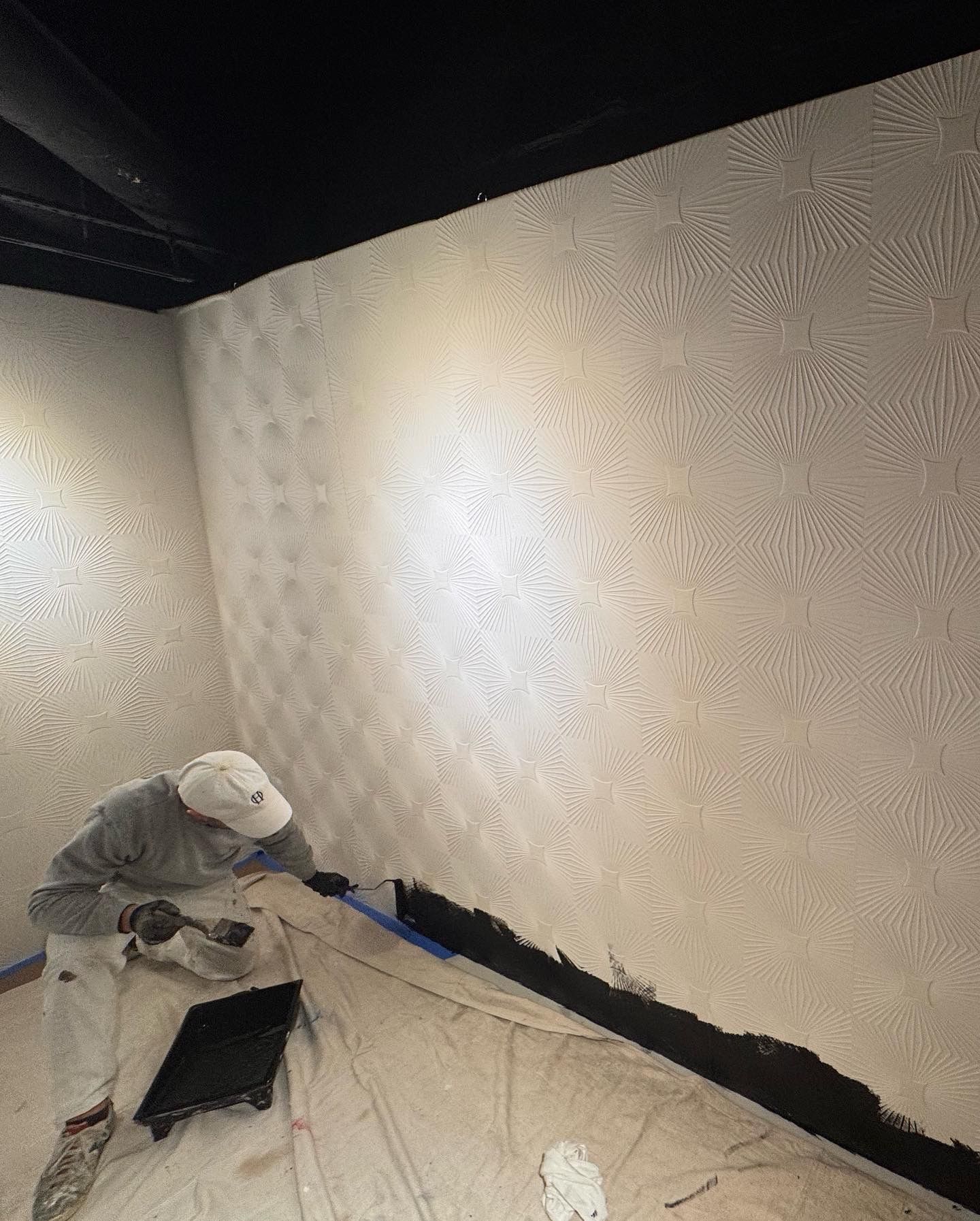 Painter applies black accent to white geometric textured mural.