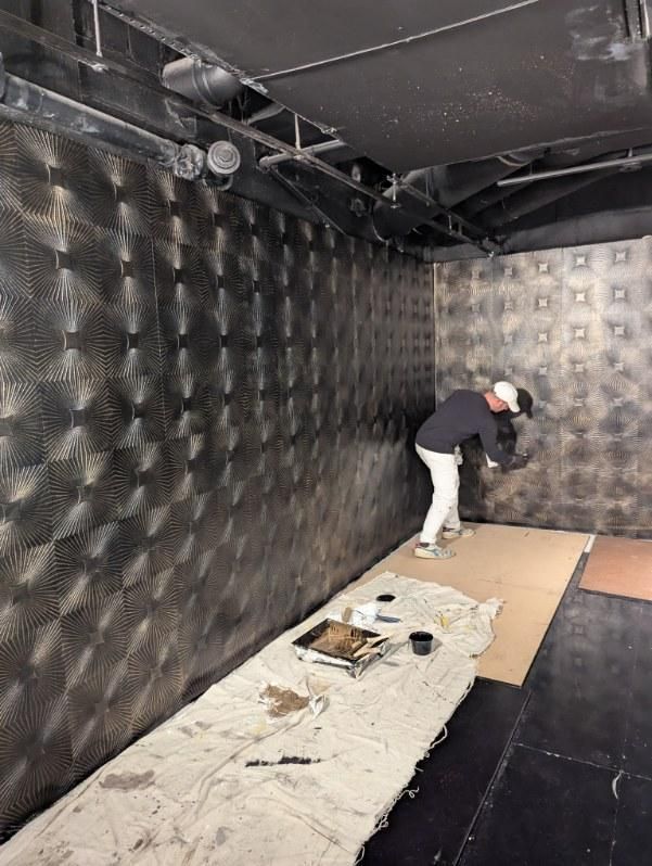 Mural install: dark upholstered wall with painting supplies below.