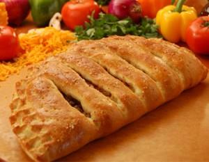 A calzone is sitting on a wooden table next to vegetables.