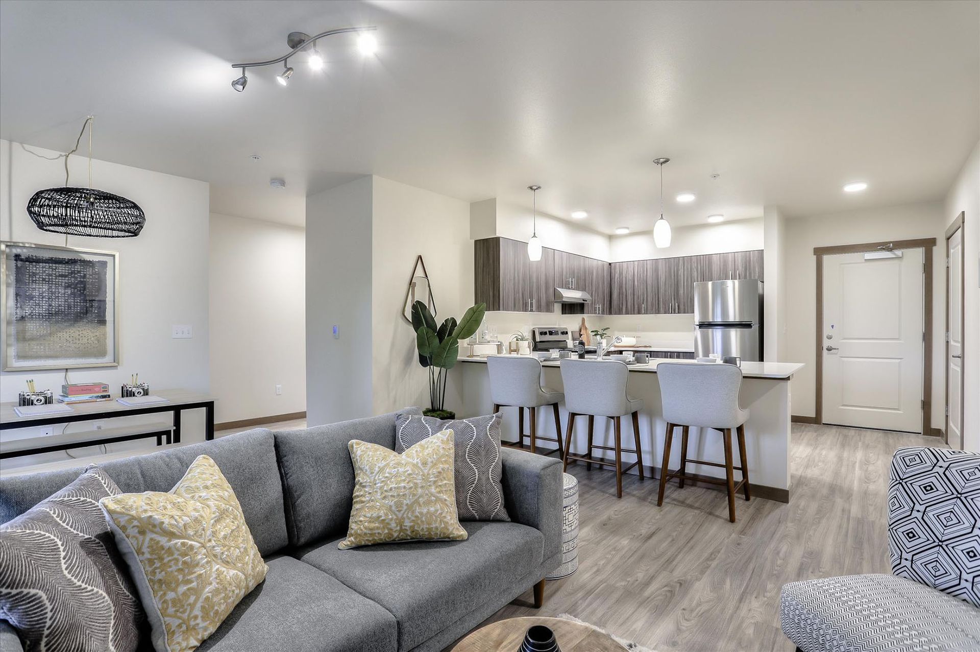 Modern apartment living room with gray sofa, open kitchen, and neutral color scheme.
