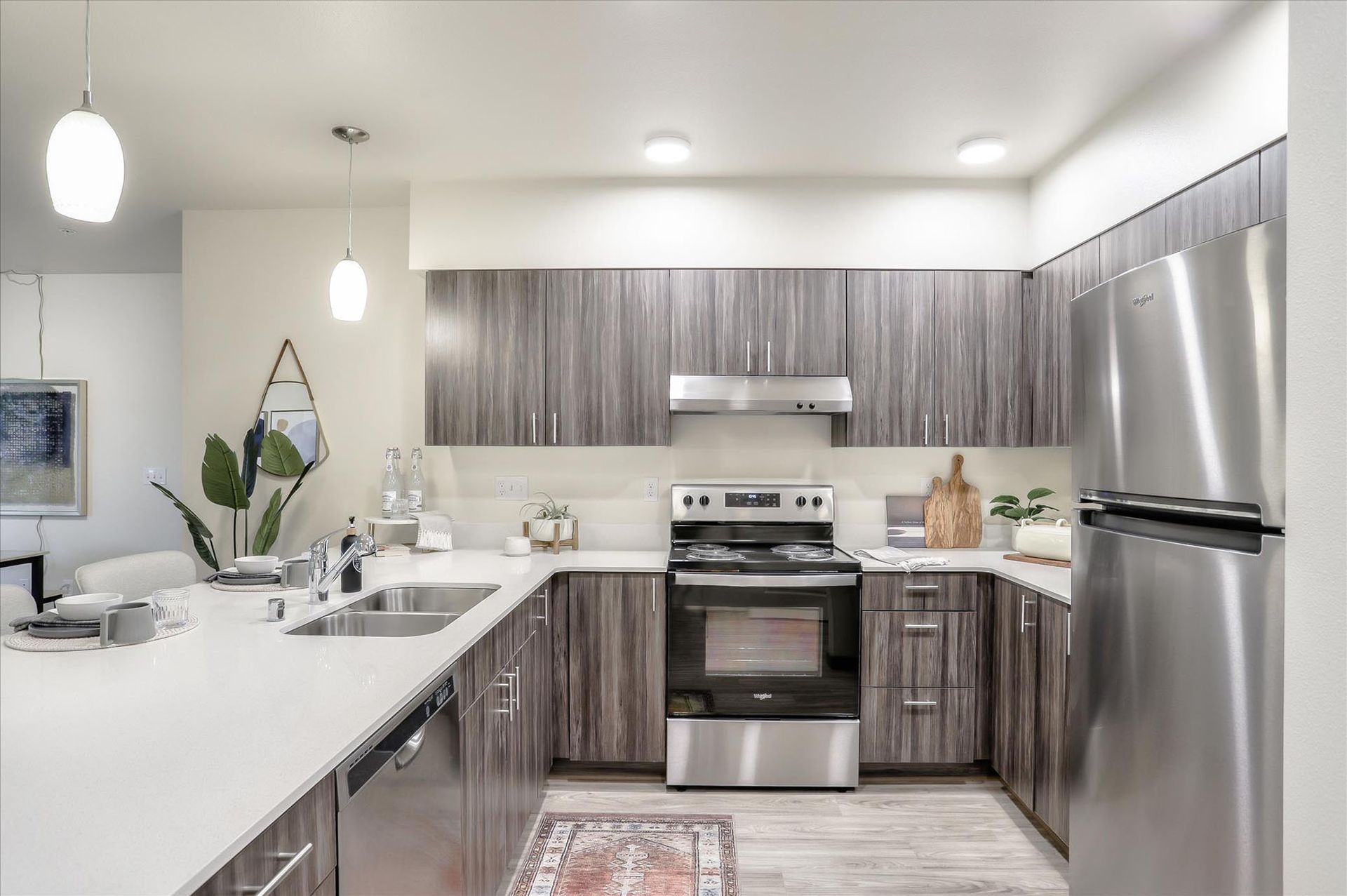 Modern kitchen with stainless steel appliances, light countertops, and dark wood cabinets.