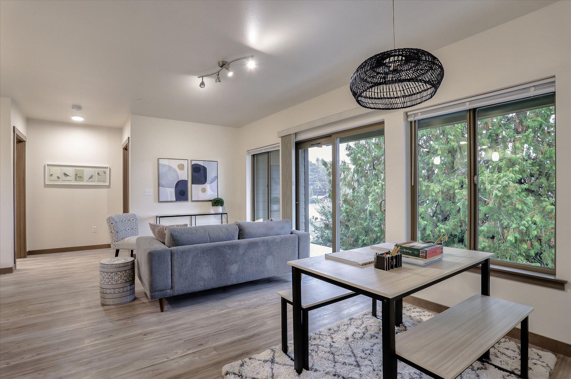 Living room with gray sofa, dining table, and large windows overlooking trees.