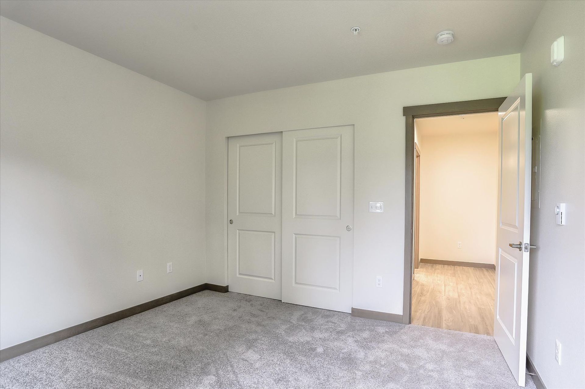 Empty bedroom with carpet, a closet, and an open doorway to another room. Neutral color palette.