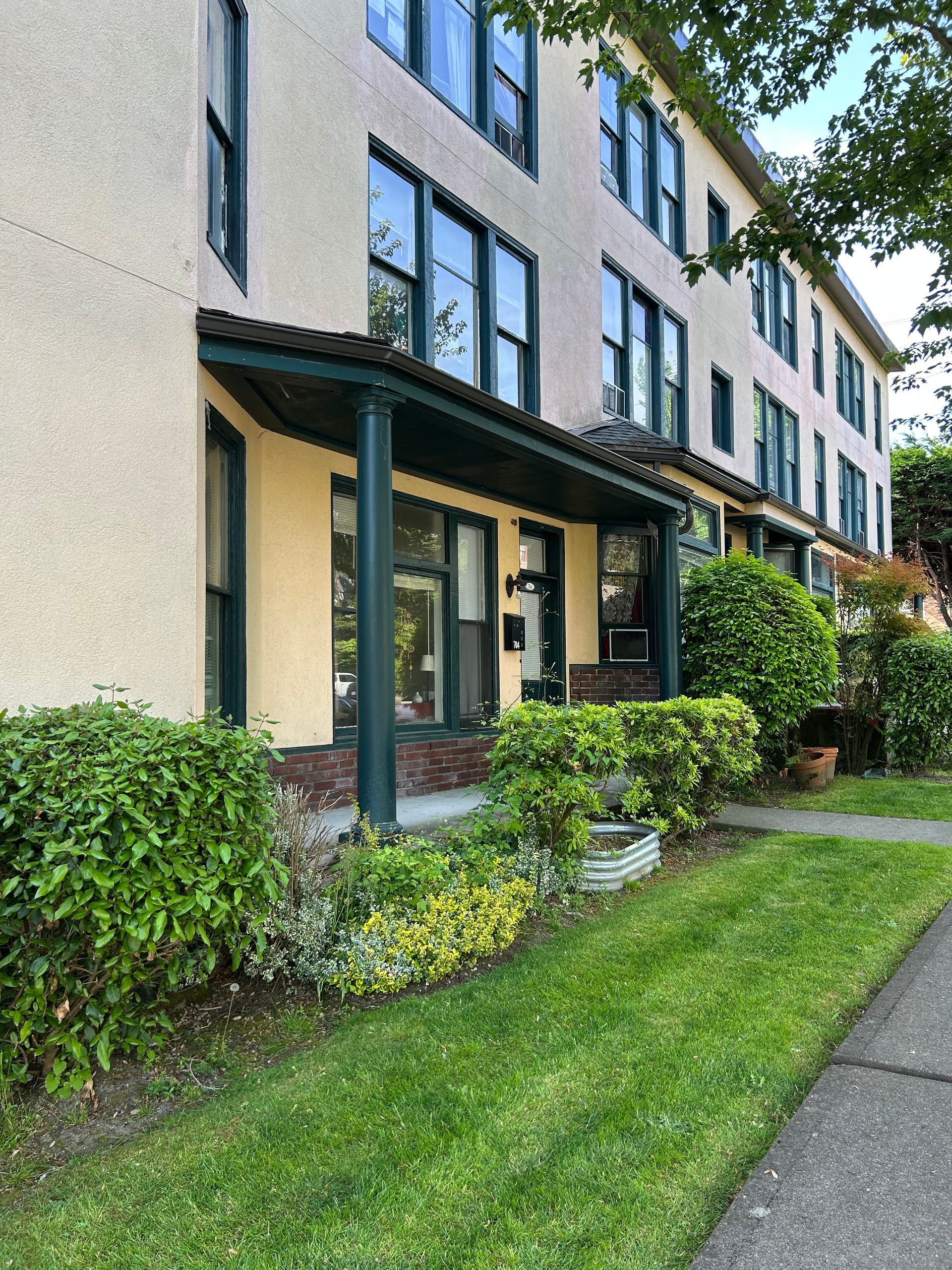 A large apartment building with a porch and a sidewalk in front of it.