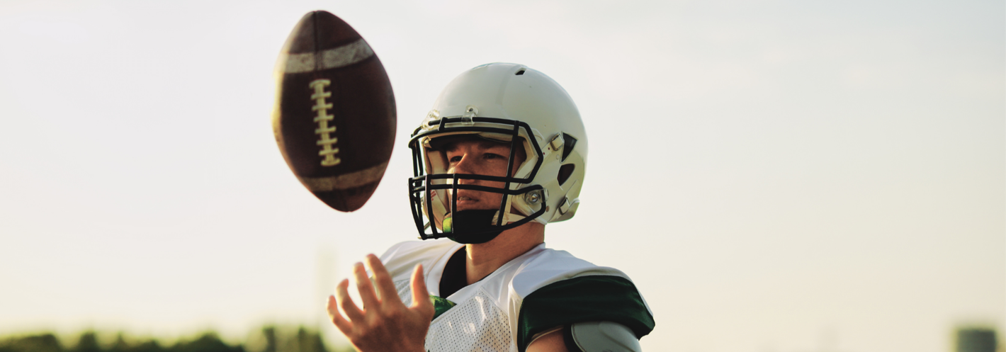 Football player, white helmet and uniform, tossing football in the air on field.
