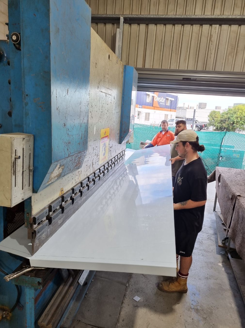 Two Workers Bending A Large White Sheet Of Material — Sheetmetal Improvements & Design in Yatala, QLD