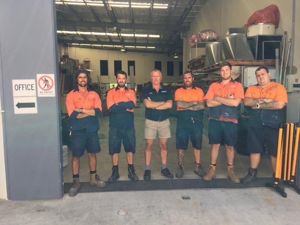 Six Workers Stand With Crossed Arms Outside a Workshop — Sheetmetal Improvements & Design in Burleigh Heads, QLD