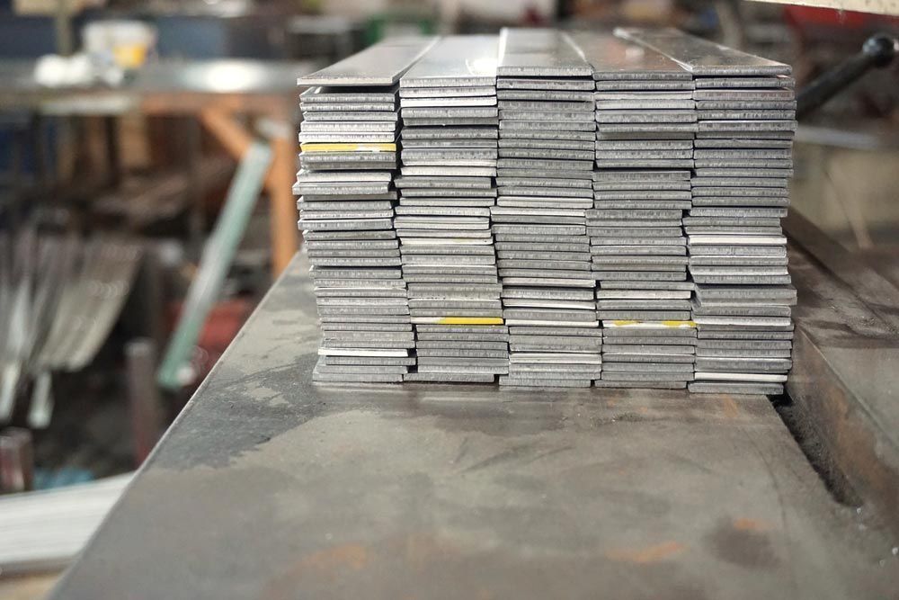 Stack of Flat Metal Bars on a Metal Surface in a Workshop — Sheetmetal Improvements & Design in Burleigh Heads, QLD