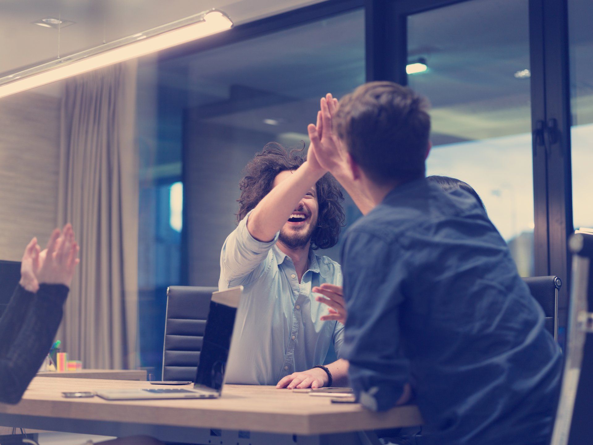 Two people giving each other a high-five at a table in an office, celebrating a success.
