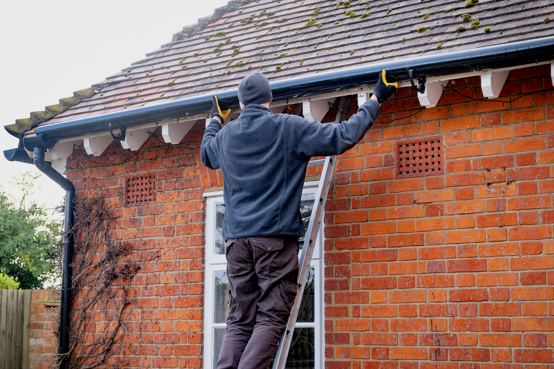 Person on ladder cleaning gutters of a brick house.