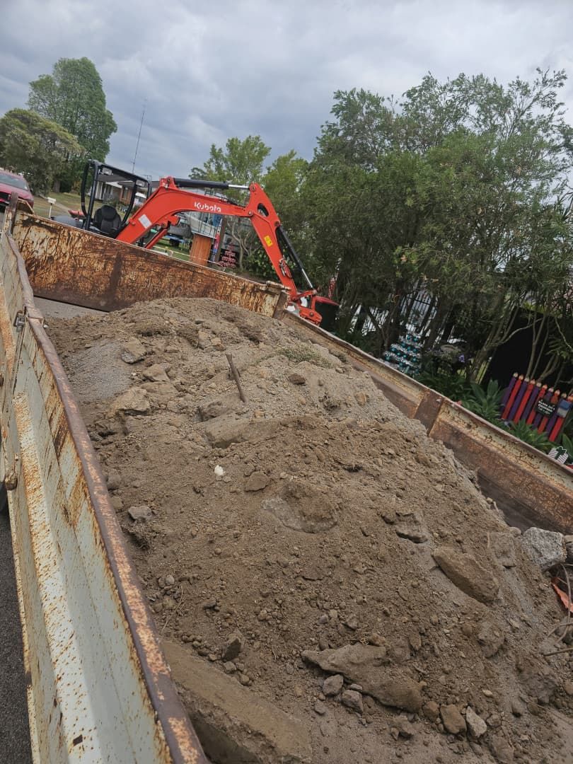 An Excavator Filling a Rusty Truck Bed With Dirt Under a Cloudy Sky — JC Excavation and Mechanical Pty Ltd in Maitland, NSW