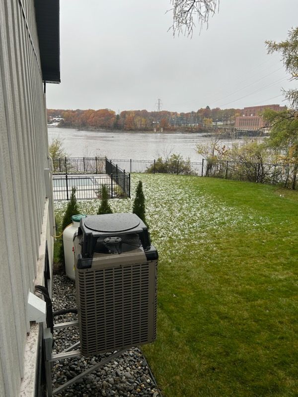 Vue arrière d'un gril, d'un réservoir de propane et d'une rivière par temps nuageux avec de l'herbe verte et une clôture.