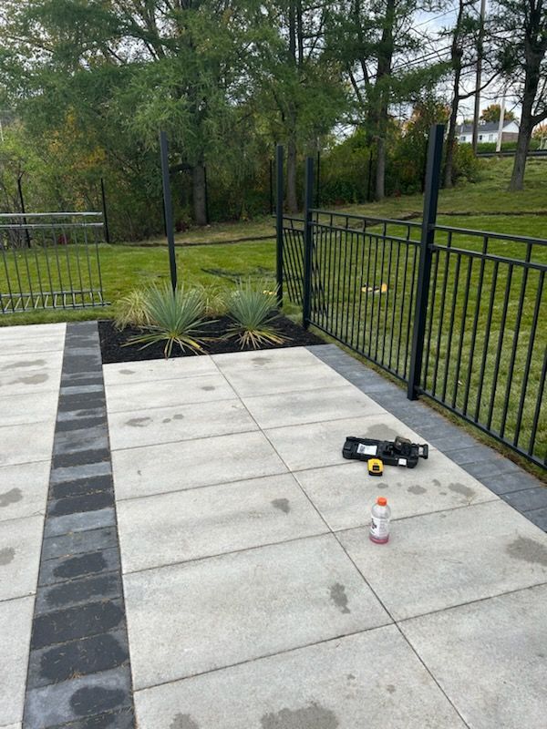 Terrasse avec pavés noirs et gris, clôture noire et aménagement paysager. Outils de construction sur la terrasse.