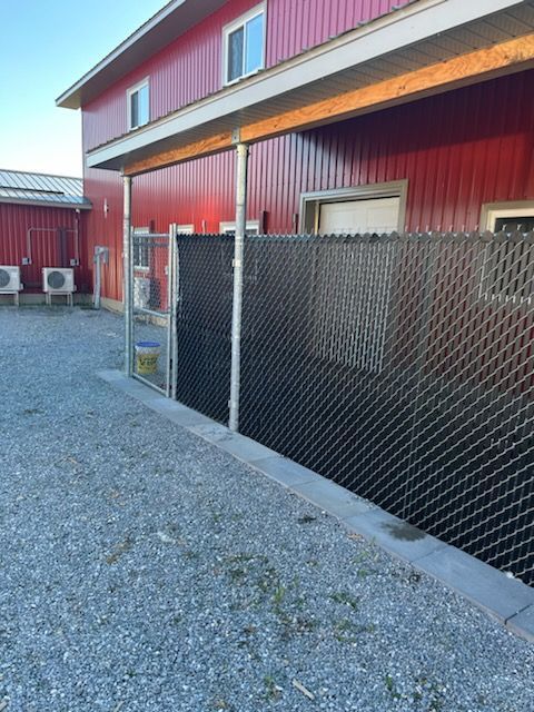 Bâtiment rouge entouré d'une clôture grillagée noire. Sol en gravier.