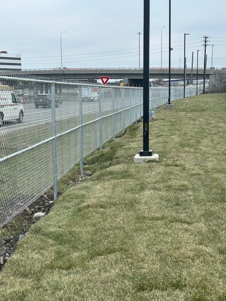 Une clôture grillagée borde une zone herbeuse à côté d'une route et d'un passage souterrain.
