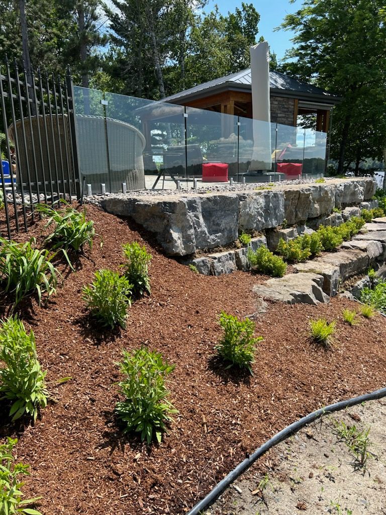 Un patio en pierre surélevé avec des balustrades en verre, des chaises rouges et un parterre de jardin rempli de plantes.