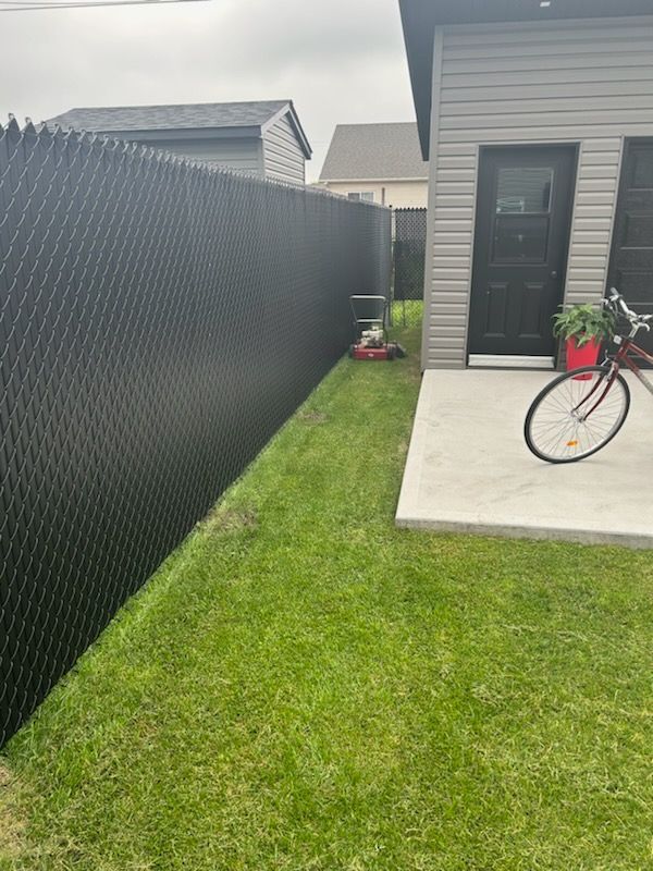 Clôture grillagée noire le long d'une pelouse verte, d'une porte de garage et d'un vélo dans une cour.