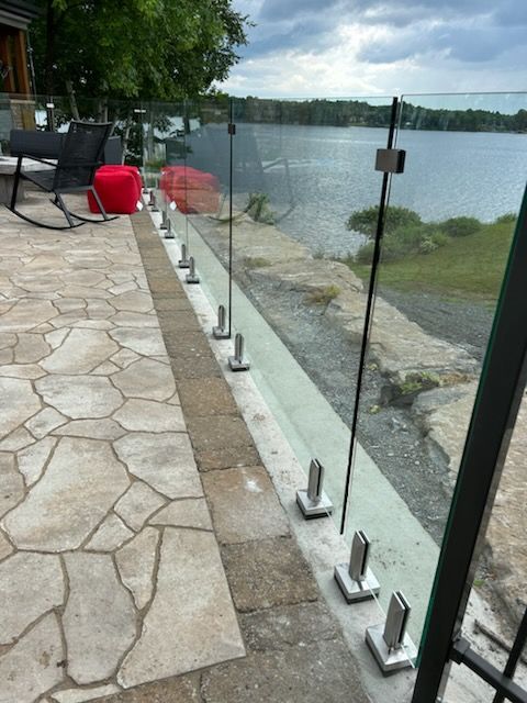 Garde-corps en verre sur une terrasse avec vue sur un lac. Poteaux en acier inoxydable et panneaux en verre transparent.