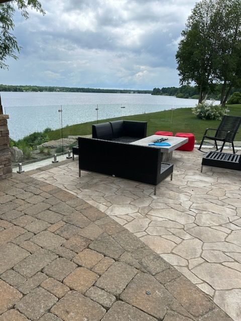 Patio avec canapé noir et vue sur le lac derrière une balustrade en verre.
