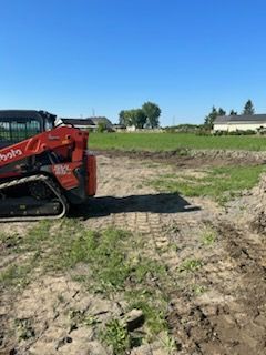 Une chargeuse sur chenilles Kubota sur terre nettoyant un champ par une journée ensoleillée.
