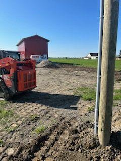 Un poteau électrique avec une chargeuse compacte dans un champ de terre à côté d'une grange rouge.