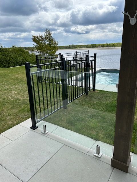 Clôture en métal noir et verre autour d'un patio avec piscine, menant à un lac.