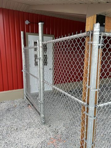 Une porte grillagée s'ouvrant sur une porte blanche, adossée à un mur de bâtiment rouge et à un sol en gravier.