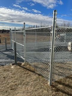 Clôture grillagée avec poteaux et portail dans un champ sous un ciel bleu nuageux.
