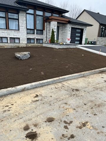 Extérieur de la maison avec pelouse fraîchement ensemencée, façade en pierre et bordure en béton.
