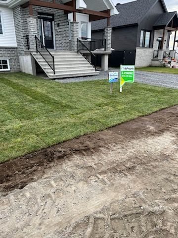 Cour avant récemment gazonnée d'une maison moderne, avec une bordure fraîchement labourée et des panneaux « À vendre ».