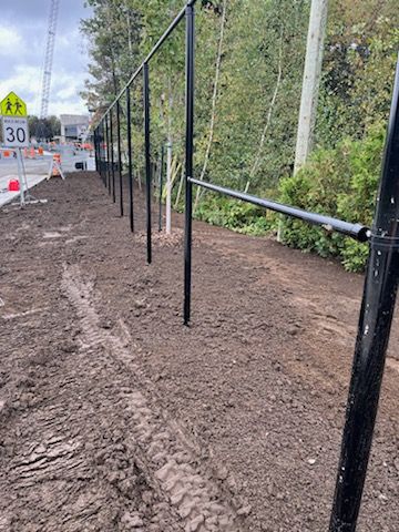 Clôture noire le long d'un chemin de terre près d'une route avec une zone scolaire.