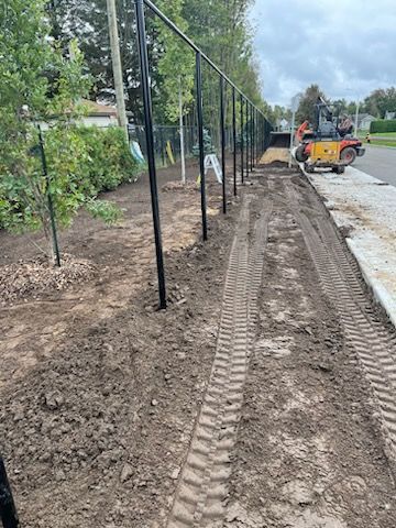 Clôture noire et engins de chantier le long d'un chemin de terre à côté d'un trottoir.