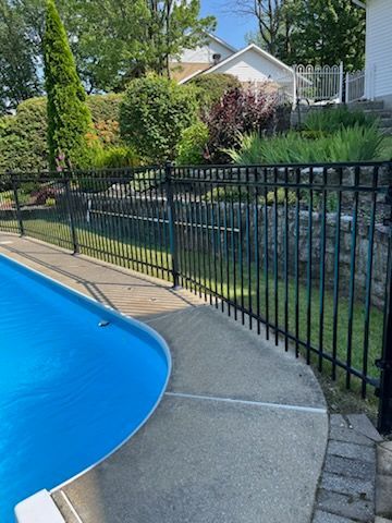 Clôture noire autour d'une piscine, la séparant d'une cour herbeuse par une journée ensoleillée.
