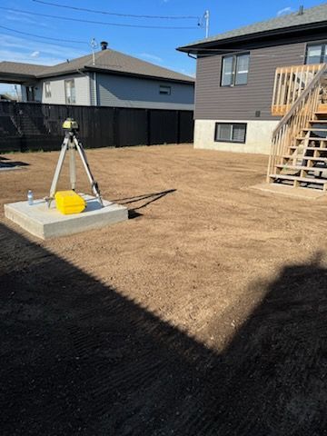 Une cour arrière avec de la terre nivelée, un instrument d'arpentage et une maison avec des escaliers.