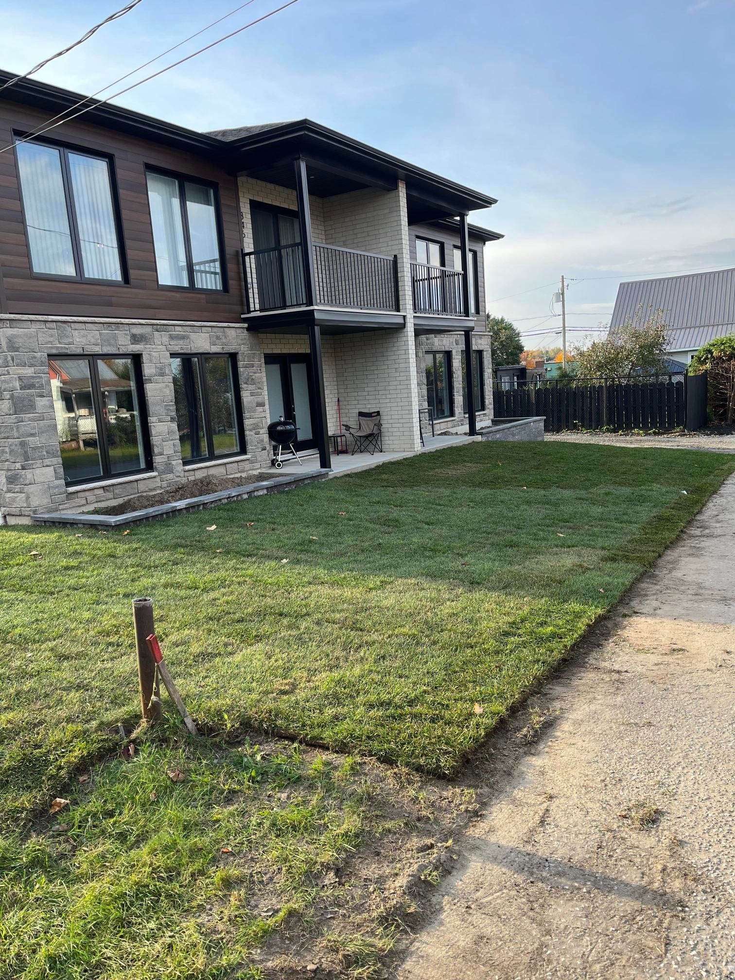Bâtiment de deux étages avec revêtement en pierre et en bois, balcons et gazon fraîchement posé dans un cadre résidentiel.
