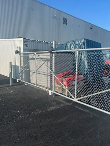 Portail grillagé, bâtiment blanc en arrière-plan, boîtes rouges visibles à l'intérieur.