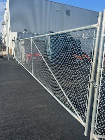 Clôture grillagée devant un bâtiment et véhicules sur l'asphalte.