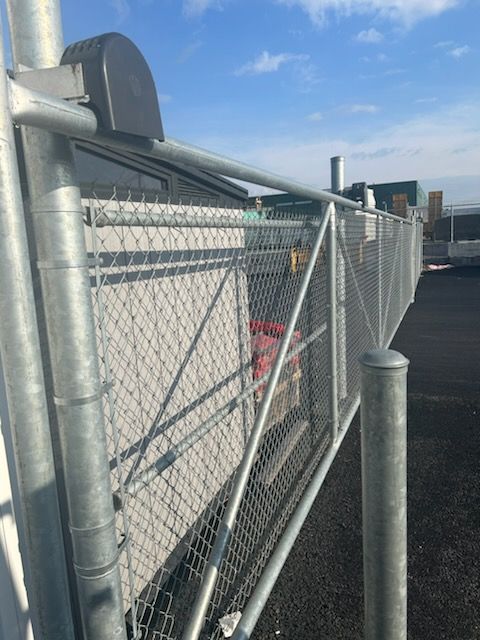 Clôture en métal galvanisé entourant une structure blanche, sous un ciel bleu.