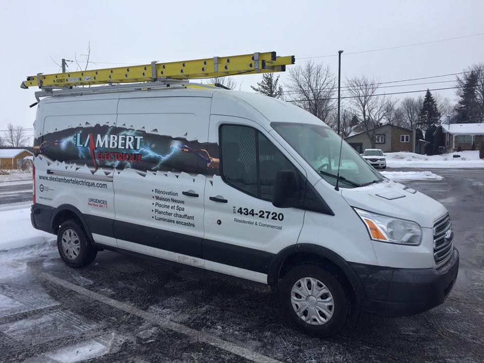 Fourgonnette électrique Lambert blanche avec échelle sur le dessus, stationnée sur un trottoir enneigé.